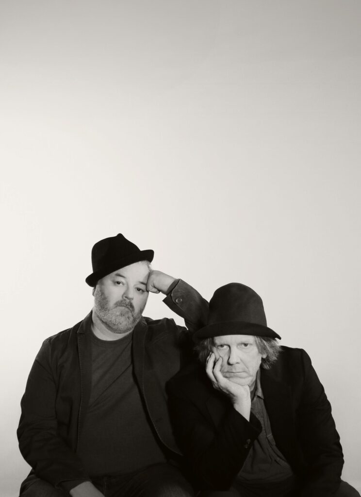 Two men in pork pie hats stare ahead glumly. One rests his chin in his hand, the other leans his head against his fist.