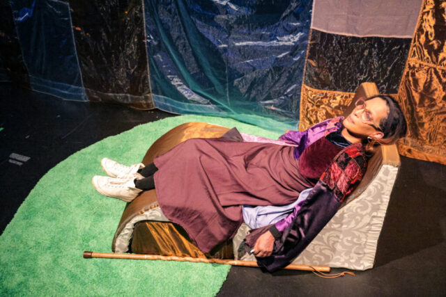 Tiresias, played by Vivi Dabee, reclines chaise long